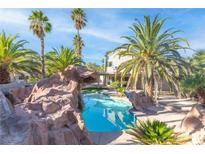 Backyard pool area featuring a rock waterfall and lush palm trees, creating a tropical oasis at 356 Clark Dr, Henderson, NV 89074