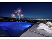 Stunning pool with lounge chairs overlooking the city skyline and fireworks display at night at 621 Majestic Rim Dr, Henderson, NV 89012