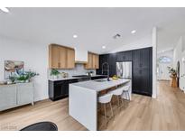 Modern kitchen featuring an island with seating, black and wood cabinets, stainless steel appliances, and wood floors at 679 Riverband Pl, Henderson, NV 89052