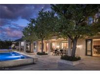 Stunning outdoor pool with stone surround, landscaped patio, and covered seating area at 1413 Iron Hills Ln, Las Vegas, NV 89134