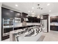 Modern kitchen featuring dark cabinetry, stainless steel appliances, and a waterfall edge island with marble-patterned countertop at 724 Step Beach St, Las Vegas, NV 89138