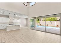 Bright living room showcasing a kitchen view and large sliding doors that open to a refreshing swimming pool area at 12048 Portamento Ct, Las Vegas, NV 89138
