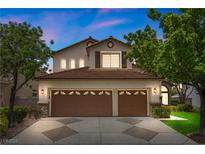 Inviting two-story home with a three-car garage, manicured lawn, and mature trees under a twilight sky at 575 Dusty Palms Ln, Henderson, NV 89052