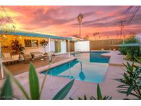 Inviting backyard pool with covered patio seating and lush greenery against a colorful sunset sky at 2043 Sombrero Dr, Las Vegas, NV 89169