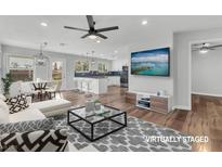 Bright, staged living room with hardwood floors, ceiling fan, modern kitchen, dining area, and an entertainment center at 1109 Maserati Dr, Las Vegas, NV 89117