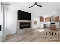 Open-concept living room with fireplace and wood-look tile flooring, and a peek into the kitchen at 10540 Beachwalk Pl, Las Vegas, NV 89144