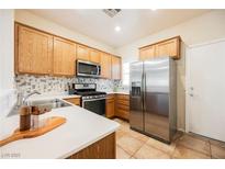 Well-lit kitchen features stainless steel appliances, white countertops, mosaic tile backsplash, and wood cabinets at 7957 Fantail Dr, North Las Vegas, NV 89084