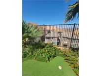 Green backyard with putting green, flowers, and views of the neighborhood beyond the metal fence at 44 Moon Hill Dr, Henderson, NV 89011