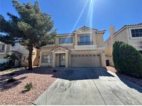 Two-story home featuring a tan exterior, two-car garage, and low maintenance rock landscaping at 10574 Salmon Leap St, Las Vegas, NV 89183