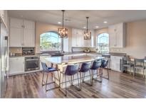 Bright open kitchen with hardwood flooring, large island with seating, modern lighting fixtures, and stainless steel appliances at 10047 Alden Creek St, Las Vegas, NV 89141