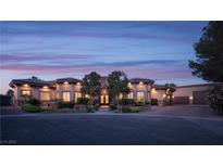 Stunning single-story home with stone accents, lush landscaping, and a circular driveway at twilight at 8620 W La Madre Way, Las Vegas, NV 89149