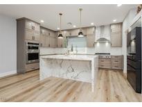 A modern kitchen featuring a marble waterfall island, stainless steel appliances, and light wood-colored cabinets at 8095 Carpenter Creek Ave, Las Vegas, NV 89113