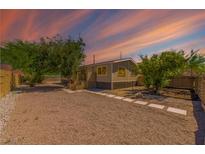 Charming single-story home with gravel landscaping, wood fence, and a beautiful desert sunset at 5822 E Carey Ave, Las Vegas, NV 89156
