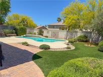 Backyard features a sparkling blue pool, lush greenery, and brick-paved patio, perfect for outdoor entertaining at 1564 Silver Knoll Ave, Las Vegas, NV 89123