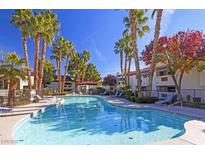 Inviting community pool surrounded by lounge chairs and lush palm trees on a sunny day at 8455 W Sahara Ave # 213, Las Vegas, NV 89117