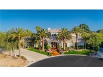 Elegant two-story house featuring a tile roof, lush landscaping, and a circular driveway with mature palm trees at 7625 Coley Ave, Las Vegas, NV 89117