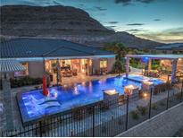 A gorgeous pool with fire pits and lounge chairs surrounded by a black fence sits in front of a hillside at 11238 Rebel Dome Ct, Las Vegas, NV 89141