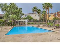 Relaxing community pool with lounge chairs and covered seating area surrounded by lush landscaping and palm trees at 9303 Gilcrease Ave # 1002, Las Vegas, NV 89149