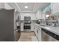 Updated kitchen boasts stainless steel appliances, white cabinets, black hardware, and patterned tile backsplash at 2507 Albemarle Way, Henderson, NV 89014