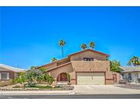 Charming stucco home with a two-car garage, palm trees, and colorful landscaping at 4475 Harmony Ct, Las Vegas, NV 89121
