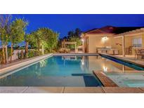 A backyard pool and spa surrounded by lush landscaping and an outdoor kitchen at dusk at 6230 Calm Brook Ct, Las Vegas, NV 89149