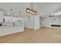 Open-concept living room with modern light fixtures, white kitchen, and sleek fireplace at 715 Taliput Palm Pl, Henderson, NV 89011
