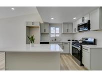 Modern kitchen boasts white cabinets, stainless steel appliances, and a center island with a white countertop at 706 Greenway Rd, Henderson, NV 89002