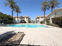 Community pool surrounded by palm trees and lounge chairs for relaxing, set between apartment buildings at 1881 W Alexander Rd # 2129, North Las Vegas, NV 89032