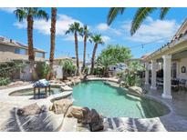 Backyard pool featuring lush palm trees, rock waterfall, and covered patio with an outdoor dining area at 8224 Fawn Meadow Ave, Las Vegas, NV 89149