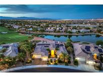 Stunning aerial view of a lakeside property with a golf course and city lights in the background at twilight at 5162 Estasi St, Las Vegas, NV 89135