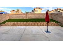 Well-kept backyard featuring a concrete patio, stone retaining wall, synthetic grass, and block fence at 2813 Painted Rose Ln, Henderson, NV 89074