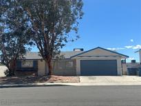 Charming single-story home featuring a two-car garage, a lush tree in the front yard, and a blue and beige color scheme at 6905 Singing Dunes Ln, Las Vegas, NV 89145