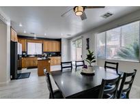Open kitchen with wood cabinets and a black island adjacent to a formal dining area with black table at 11004 Napa Ridge Dr, Las Vegas, NV 89144