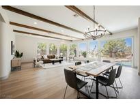Open living and dining area featuring exposed wood beams, chandelier, and large windows with outdoor views at 2177 Magnolia Pond Ct, Henderson, NV 89052