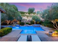 Inviting backyard pool and spa with rock wall feature, lush landscaping, and lounge chairs at 900 Cantura Mills Rd, Henderson, NV 89052