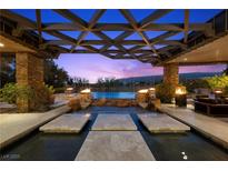 Stunning outdoor pool area featuring fire pits, stone accents, and a covered lounge space, perfect for evening relaxation at 11 Golden Sunray Ln, Las Vegas, NV 89135