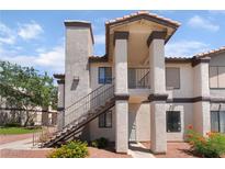 Two-story condo featuring stairs, red gravel landscaping, and tan stucco with dark trim at 1575 W Warm Springs Rd # 2822, Henderson, NV 89014