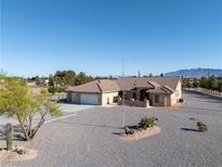 Wide shot of a desert home with gravel landscaping, a three-car garage, and a mountain view at 1361 Moose St, Pahrump, NV 89048