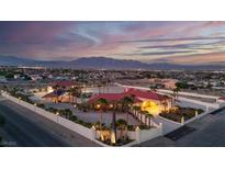 Expansive estate with red tile roof, palm trees, a pool, set against a stunning mountain backdrop at dusk at 10280 W La Mancha Ave, Las Vegas, NV 89149