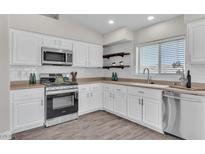 Bright kitchen featuring white cabinets, stainless steel appliances, subway tile backsplash, and wood-look flooring at 7820 Milkweed Ct, Las Vegas, NV 89149