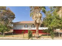 Charming two-story home with white balcony, red trim, and a desert landscape with mature trees in front at 2855 Rice St, Logandale, NV 89021