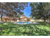 Beautiful backyard featuring a sparkling pool, lush green grass, mature trees and an outdoor cooking area at 7460 Buckskin Ave, Las Vegas, NV 89129