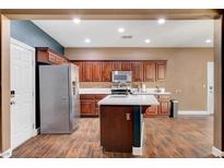Well-lit kitchen features wood cabinetry, stainless steel appliances, an island, and wood-style floors at 8560 Alocasia Ct, Las Vegas, NV 89149