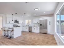 Bright kitchen features white cabinets, stainless steel appliances, a breakfast bar, and wood-look flooring at 6420 Rosemount Ave, Las Vegas, NV 89156