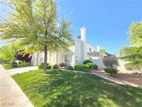 Landscaped front yard with green lawn, mature trees, and a charming white home under a clear blue sky at 451 Rumford Pl, Henderson, NV 89074