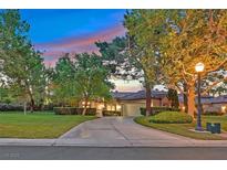 Inviting home exterior with a lush lawn, mature trees, and a circular driveway leading to an attached two-car garage at 8370 Plum Creek Ct, Las Vegas, NV 89113
