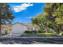 Charming single-story home featuring a lush green lawn, mature trees, and a two-car garage at 8981 Rivers Edge Dr, Las Vegas, NV 89117