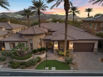 Stunning desert home with a stone turret, lush landscaping, and a tile roof set against a mountain backdrop at sunset at 51 Avenida Sorrento, Henderson, NV 89011