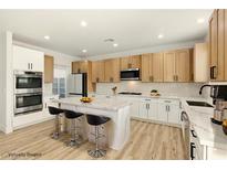 Modern kitchen features stainless steel appliances, light wood cabinets, and island with white countertop and bar stool seating at 10302 Artful Stone Ave, Las Vegas, NV 89149