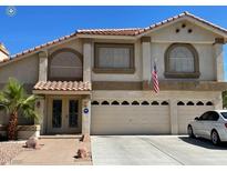 Two-story home featuring a three-car garage, an American flag, a desert landscape, and a tile roof at 4542 Amber Canyon Ln, Las Vegas, NV 89129